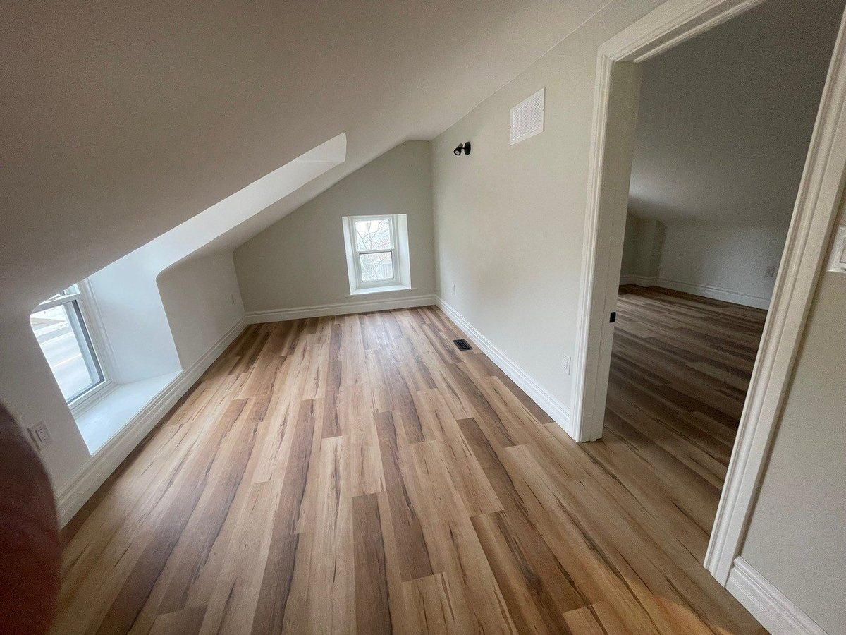 Empty attic bedroom with hardwood flooring, sloped ceilings, small window, and doorway leading to adjacent room