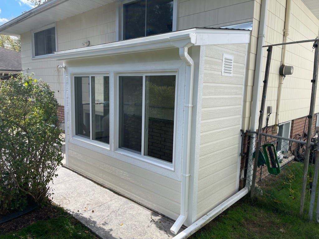 White shed with large windows attached to house exterior next to metal gate
