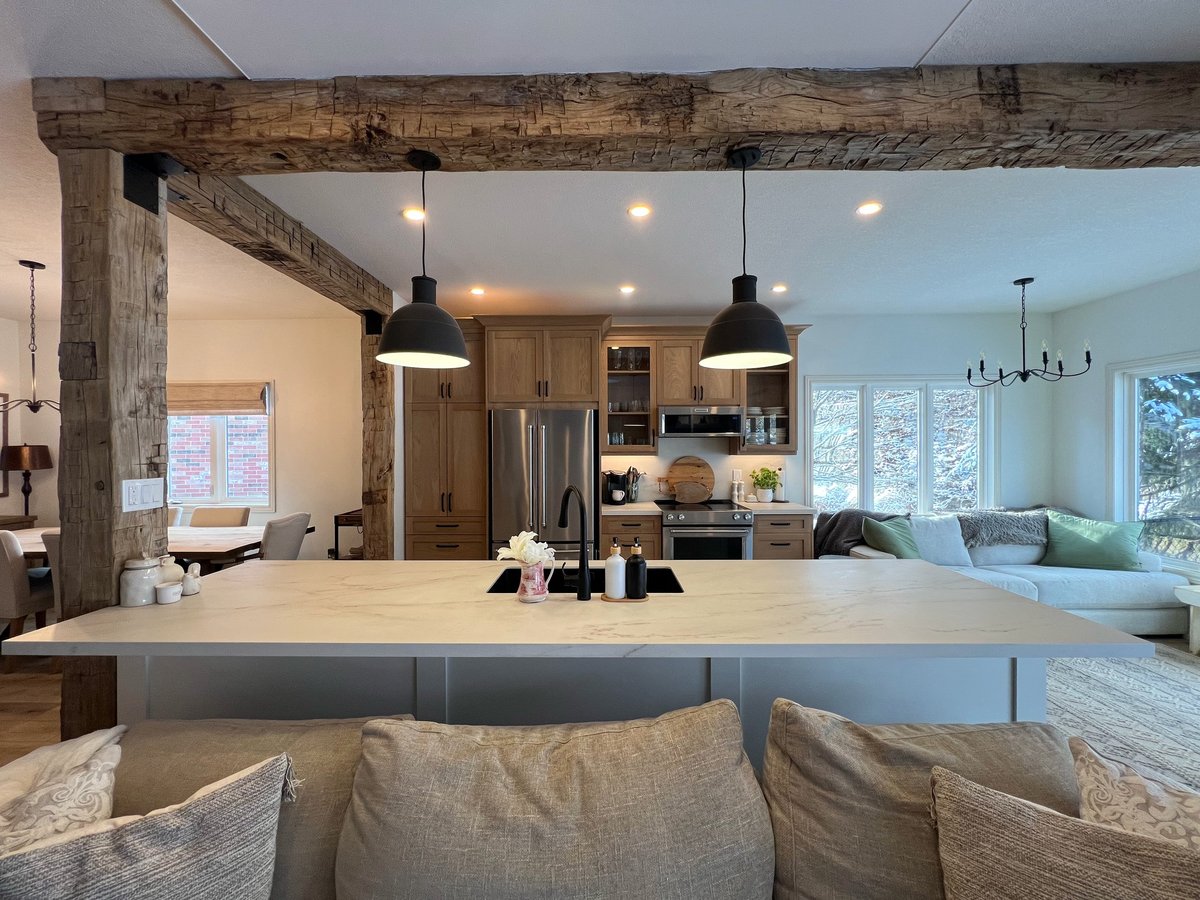 Modern open-concept kitchen and living room with exposed wooden beams, large island countertop, pendant lights, and comfortable seating area