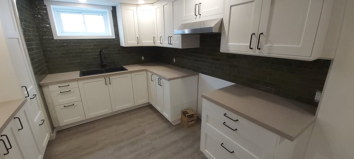 Modern kitchen with white cabinetry, black countertops, and dark tile backsplash under renovation