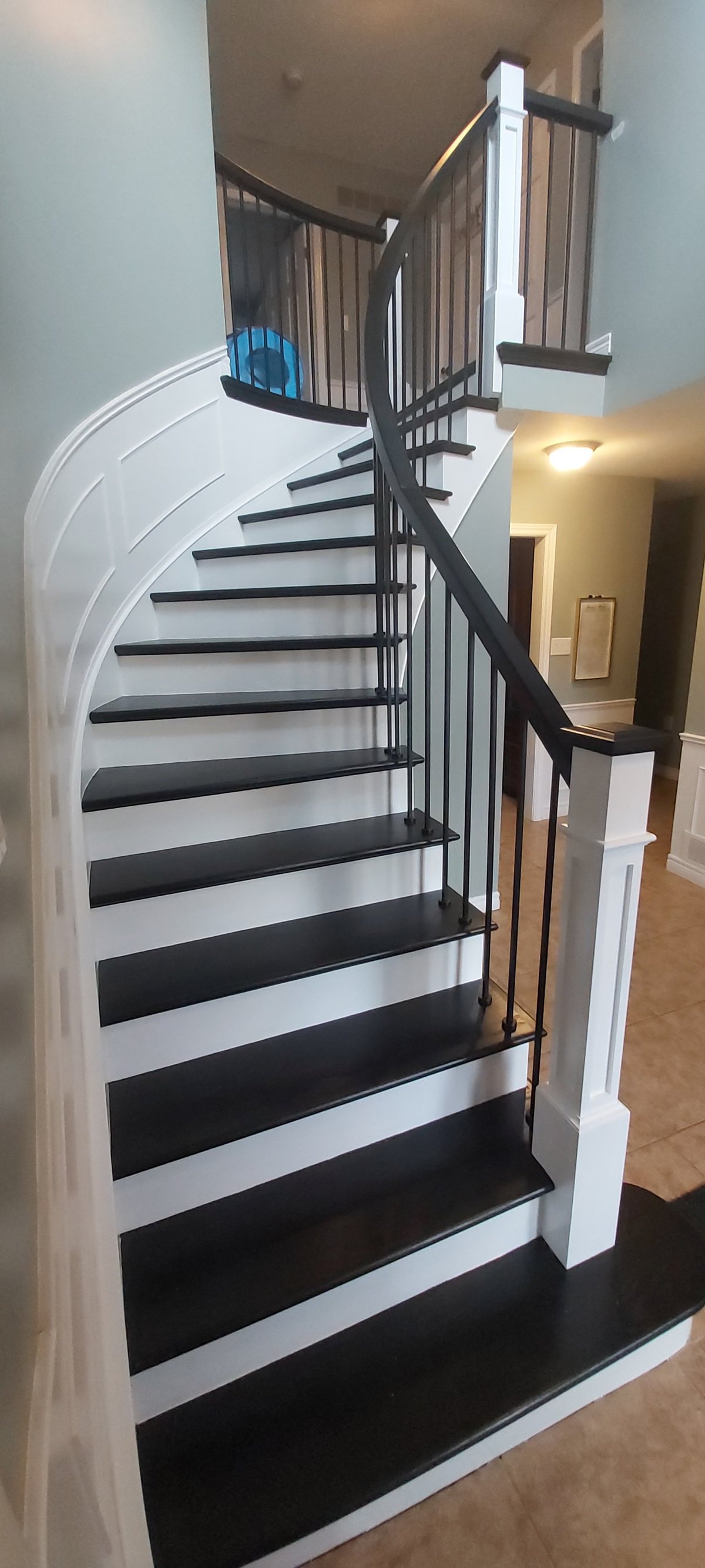 Modern curved staircase with black steps, white risers, and black metal railings leading upward in a contemporary home