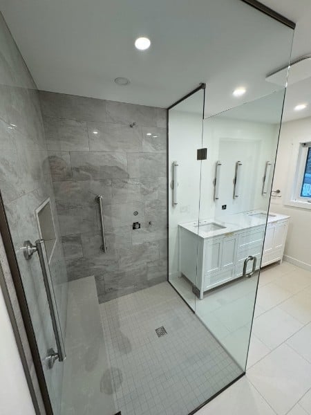 Modern bathroom with large glass-enclosed shower, white vanity sink, and marble tile accents