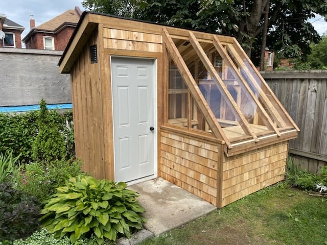 Wooden garden shed with white door and angled glass panels, located in a residential backyard