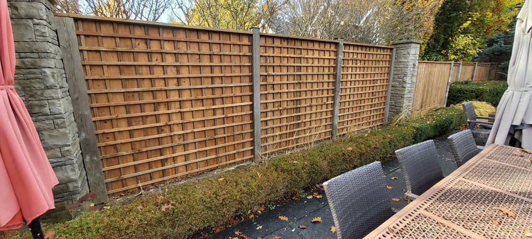 Wooden lattice fence panels with stone pillars in a residential backyard with paved patio area