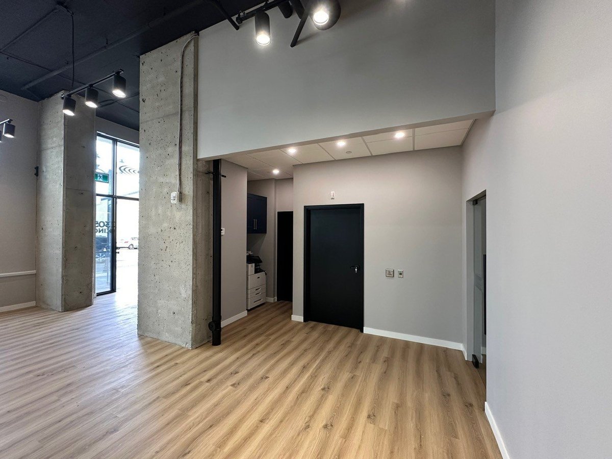 Modern empty commercial space with exposed concrete column, wooden flooring, white walls, and recessed lighting