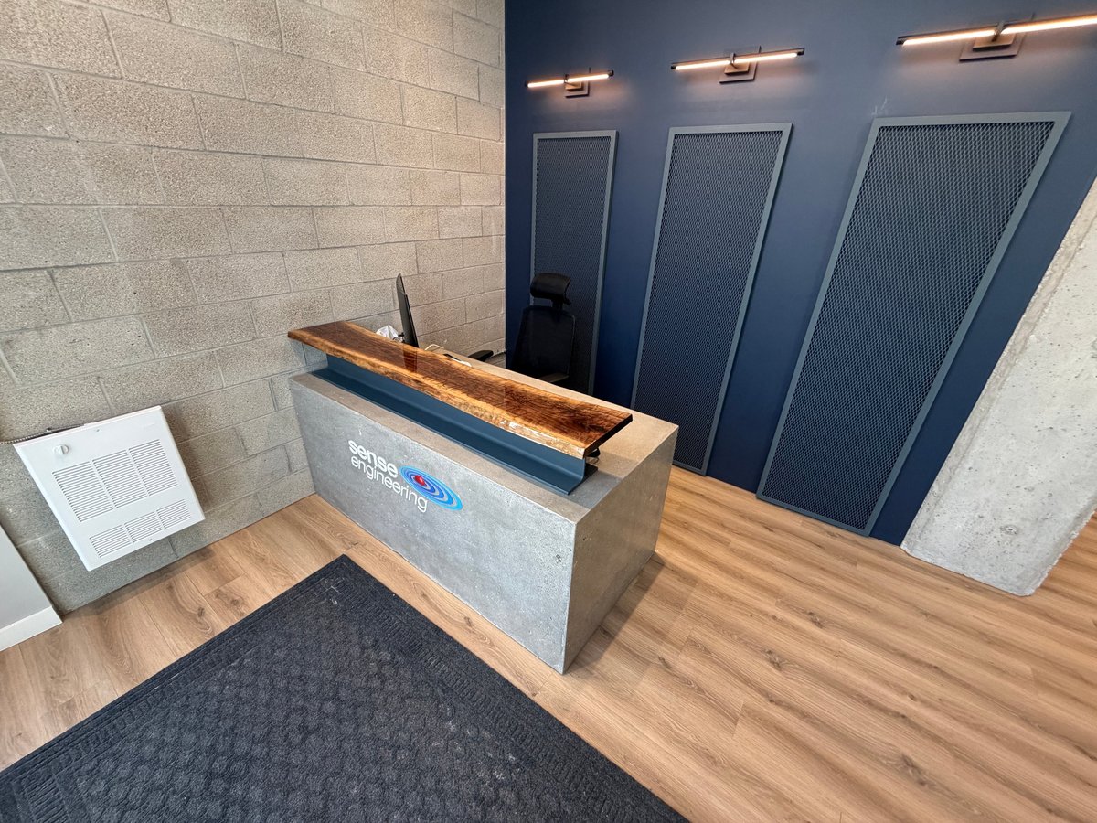 Modern office lobby with concrete reception desk, wooden top, live plant, and three closed dark doors with pendant lights above