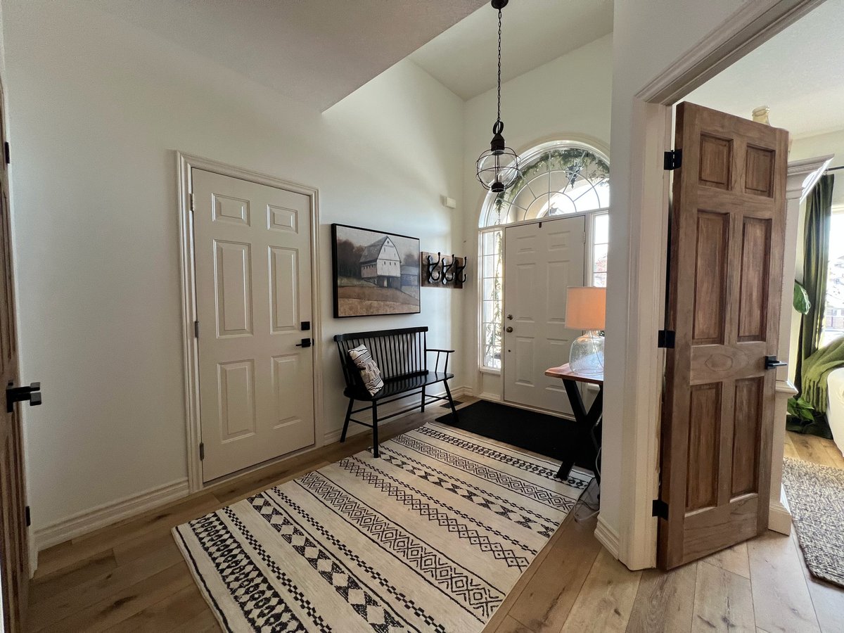 Bright entryway with patterned rug, wooden doors, black rocking chair, pendant light, and transom window above the doorway