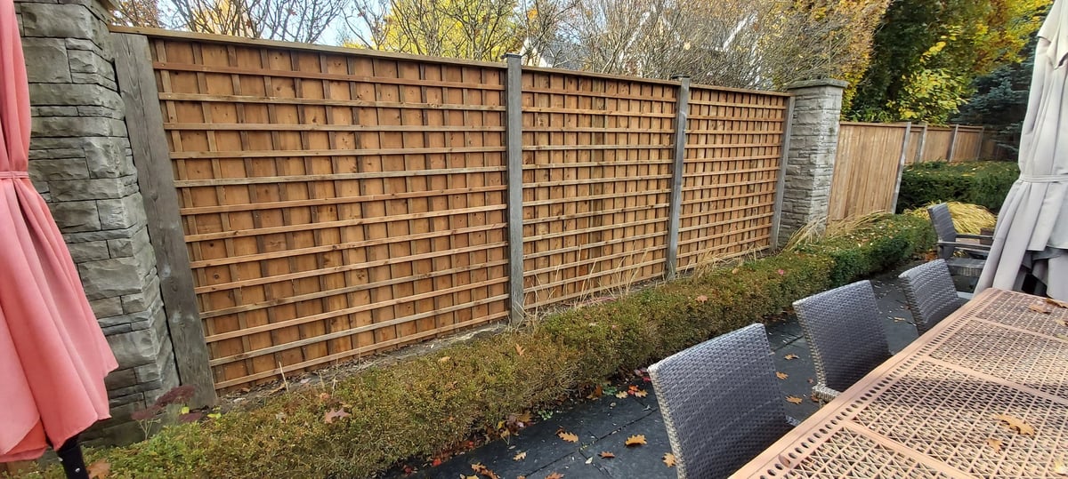 Brown lattice fence panels in a garden setting with stone pillars and patio flooring visible on the right side