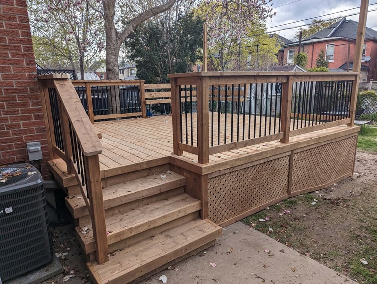 Wooden elevated deck with stairs, railings, and lattice skirting attached to a brick house in a residential neighborhood