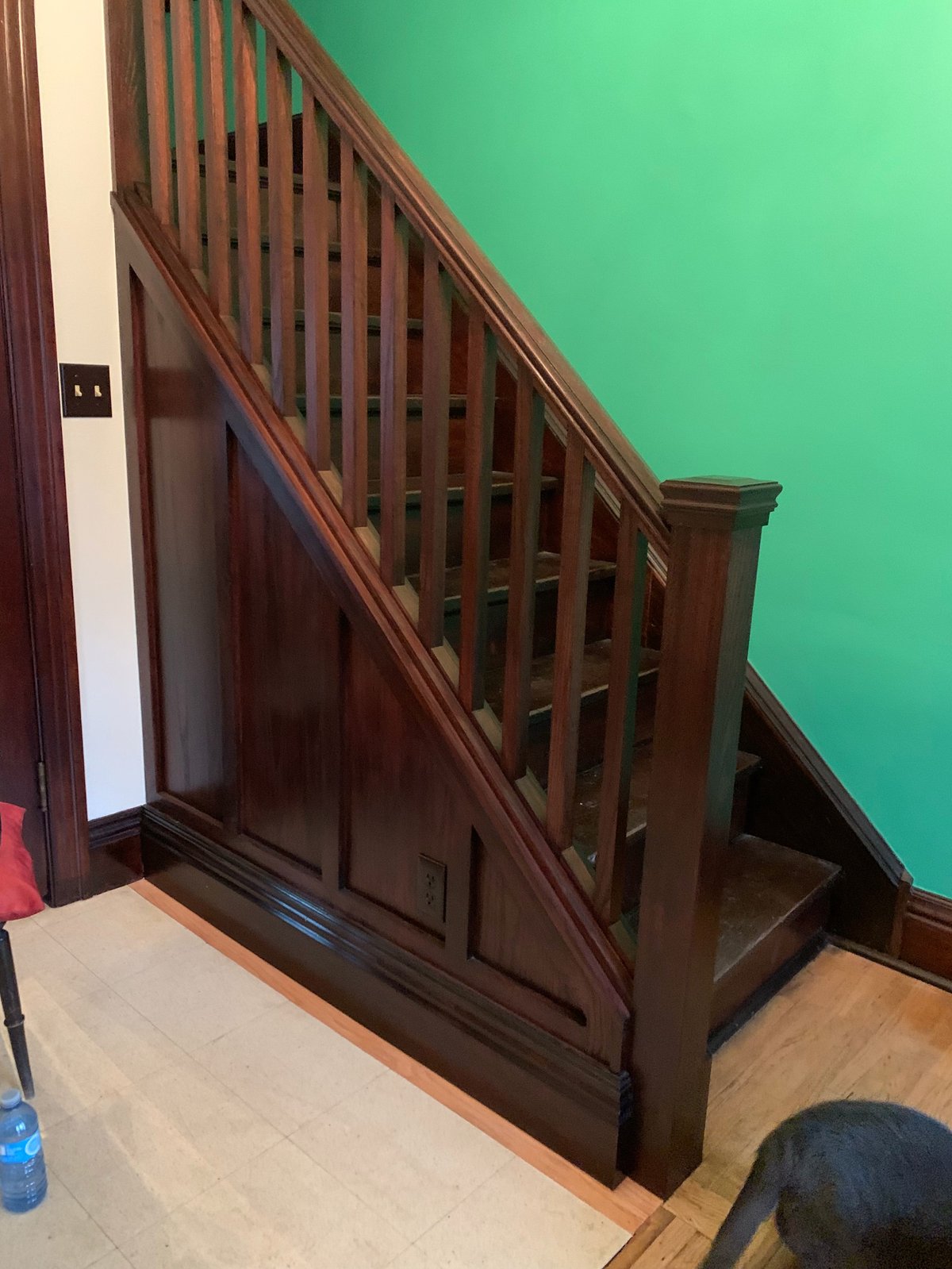 Interior staircase with dark wood railings against a bright green wall, beige tiled floor, and white trim